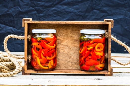 Wooden crate with glass jars with pickled red bell peppers.Preserved food concept, canned vegetables isolated in a rustic composition.