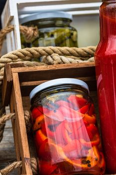 Glass jars with pickled red bell peppers and bottles with tomatoes sauce isolated in a rustic composition. Jars with variety of pickled vegetables preserved food concept.