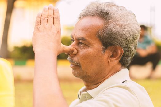 Closeup of of senior man doing alternate Nostril Breathing exercise or nadi shodhana pranayama at park - Concept of healthy active old people lifestyle