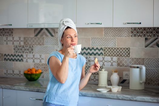 Happy Girl with a towel on her head sutra drinks coffee with cookies for breakfast in his own kitchen