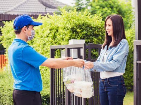 Asian young delivery man wear face mask he making grocery service giving rice food boxes plastic bags to woman customer receiving door at house after pandemic coronavirus, Back to new normal concept