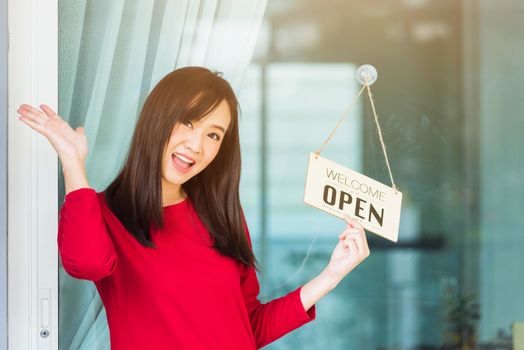 Asian young woman glad and smiling she notice sign wood board label "WELCOME OPEN" hanging through glass door front shop, Business turning open after coronavirus pandemic disease, back to new normal