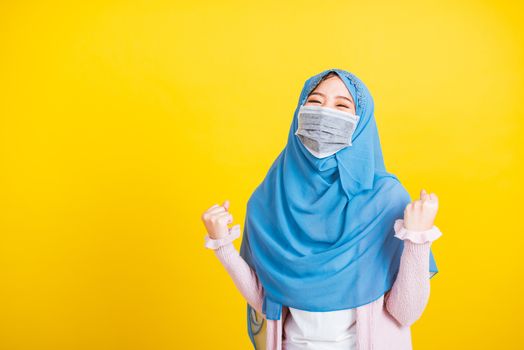 Asian Muslim Arab, Portrait of happy beautiful young woman Islam wear veil hijab and face mask protect raise hands glad excited cheerful after recovering from illness coronavirus isolated yellow