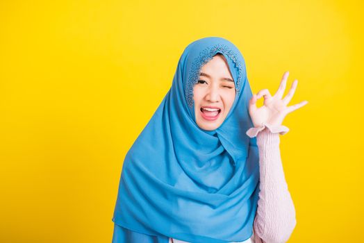 Asian Muslim Arab, Portrait of happy beautiful young woman Islam religious wear veil hijab funny smile she showing gesture fingers in okay gesture symbol, OK sign isolated yellow background