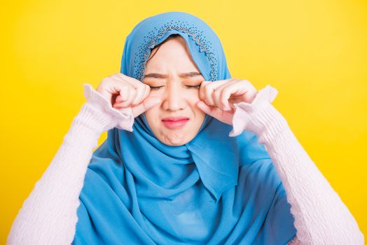 Asian Muslim Arab, Portrait of happy beautiful young woman religious wear veil hijab she sad crying using hand wiping tears in her eyes, studio shot isolated on yellow background with copy space