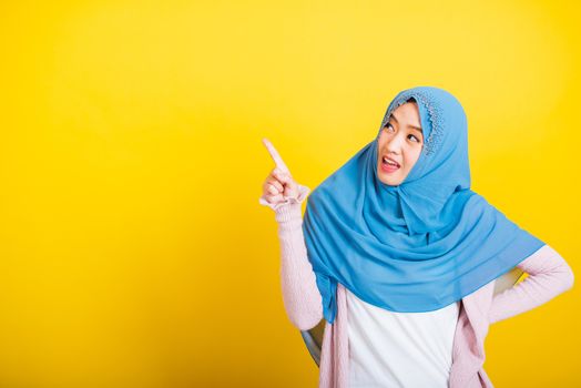 Asian Muslim Arab, Portrait of happy beautiful young woman Islam religious wear veil hijab funny smile she positive expression pointing finger side sideways to space isolated yellow background