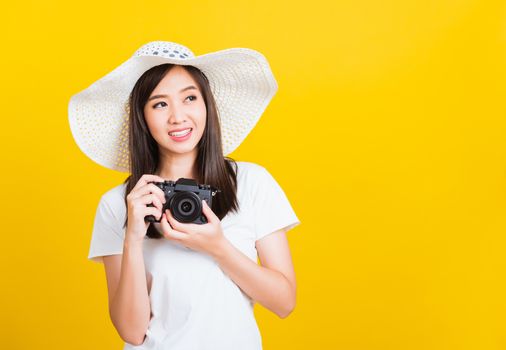 Portrait of happy Asian beautiful young woman photographer holding vintage digital mirrorless photo camera on hands, studio shot isolated on yellow background, lifestyle teenager hobby travel concept
