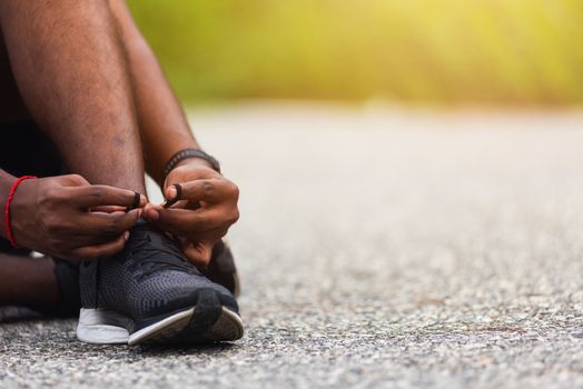 Close up Asian sport runner black man sitting shoelace trying running shoes getting ready for jogging and run at the outdoor street, health exercise workout concept