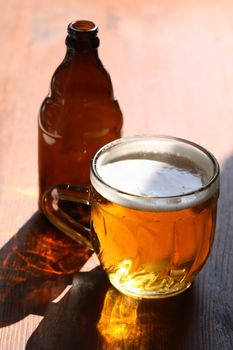 Mug of beer with foam on wooden table under sunlight