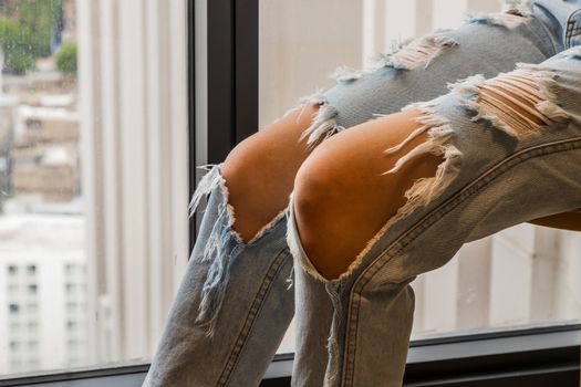 Close up of brown skin in distressed Jeans torn at the knee. Young fashionable Asia woman's legs in denim fabric for summer fashion Trendy. Selective focus.