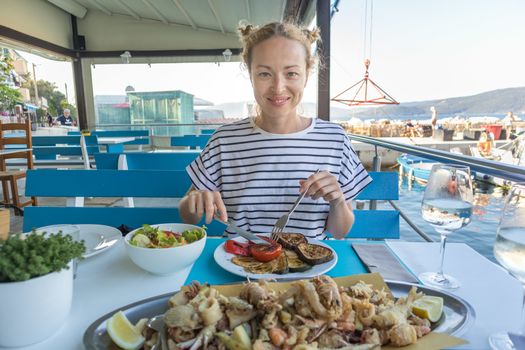 Beautiful female tourist eating delicious sea food on summer vacation in traditional croatian costal restorant by the sea.