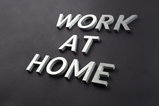 the words work at home laid with silver metal letters on matte black background in diagonal perspective, full frame view
