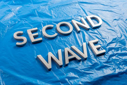 the words second wave laid with silver metal letters over crumpled blue plastic film background in slanted perspective