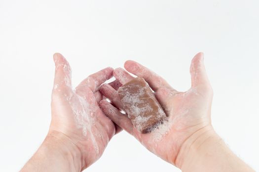 a wet piece of brown tar soap in human hands on white background.