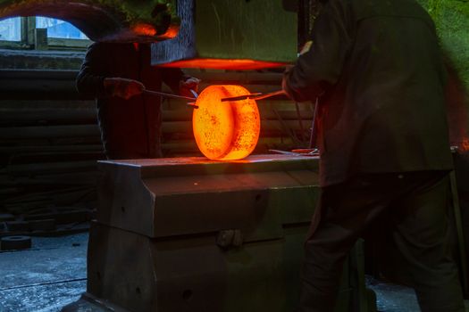 close-up picture of hot steel manual forging process with big mechanical hammer machine, sparks flying out from workpiece