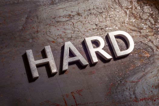 the word hard laid with silver metal letters on rusted burnt iron flat surface background in diagonal composition