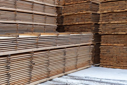 Large stacks of wooden planks background with selective focus and linear perspective. Winter woodwork industrial storage.