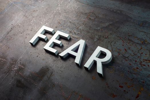 the word fear laid with silver letters on raw rusted steel sheet surface in slanted diagonal composition