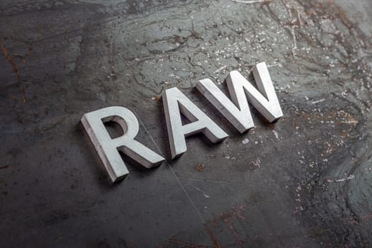 the word raw laid with silver metal letters on hot rolled steel sheet surface - close-up with selective focus and diagonal perspective