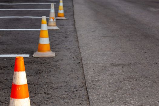 Orange road cones on a asphelt driving area with white lines, close-up with selective focus and backgropund blur.