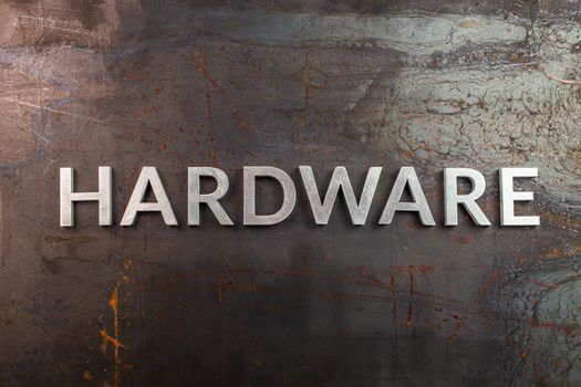 word hardware laid in with silver metal letters on rusted heavy hot rolled uncoated steel sheet surface - directly above in flat lay composition