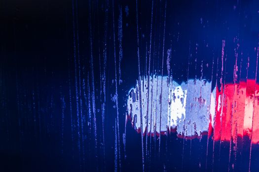 red and blue night police lights bokeh trough wet glass close-up with selective focus abstract background