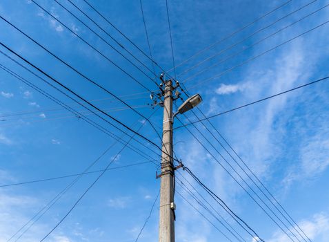 Concrete lamp post with many cables connected radially on blue sky with feather clouds in the background, Centered composition. Old electrical grid theme,