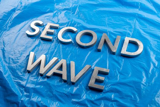 the words second wave laid with silver metal letters over crumpled blue plastic film background with diagonal descending perspective.