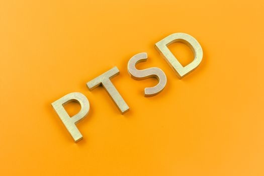 abbreviation PTSD - post traumatic stress disorder - laid with silver metal letters on yellow flat surface in ascending diagonal composition