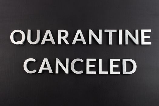 the words quarantine canceled laid with silver metal letters on matte back flat surface directly above in flat lay perspective, end of restrictions concept