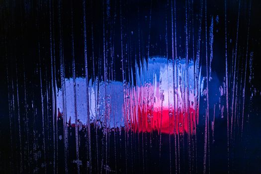 red and blue night police lights bokeh trough wet glass close-up with selective focus abstract background