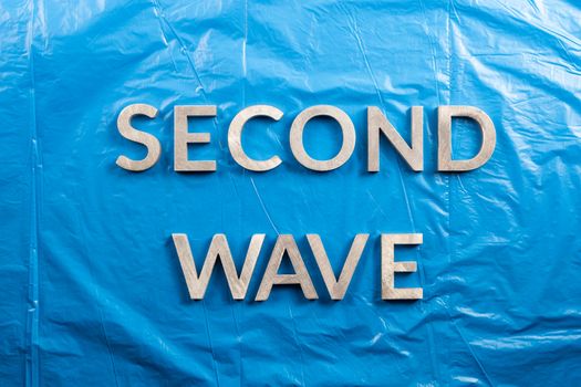 the words second wave laid with silver metal letters over crumpled blue plastic film background.
