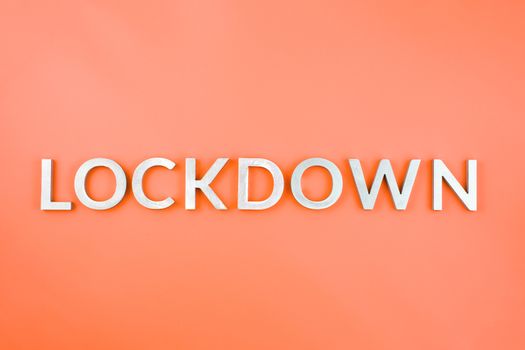 the word lockdown laid with brushed aluminium metal letters on lush lava orange color background in flat lay composition