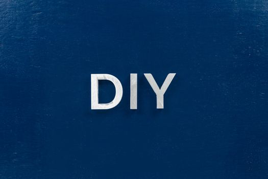 the abbreviation diy - do it yourself - laid with aluminium letters over dark blue flat surface, directly above perspective