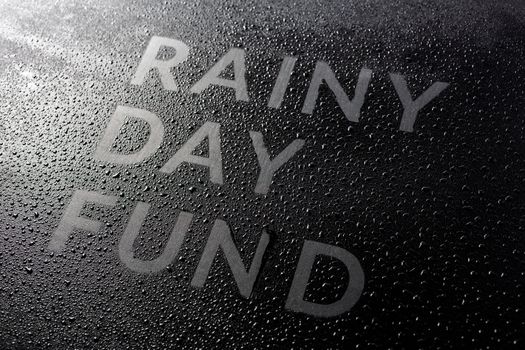 the dry words rainy day fund covered from water drops on black surface, unusual implementation concept with slanted diagonal perspective with selective focus