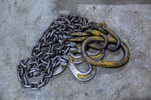 old industrial crane chain lays on concrete floor with rings and hooks.