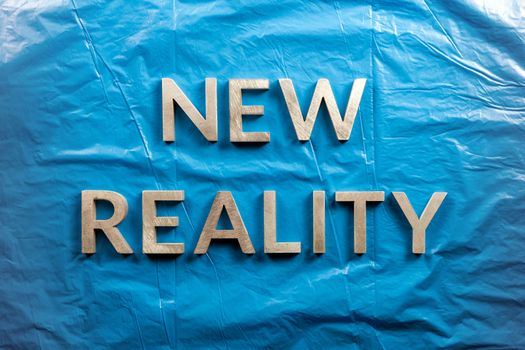 the words new reality laid with white letters over crumpled blue plastic film background in directly above perspective