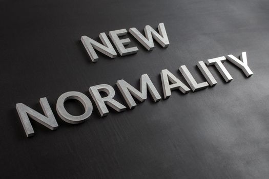 the words new normality laid with silver metal letters on flat black matte surface in slanted diagonal perspective.