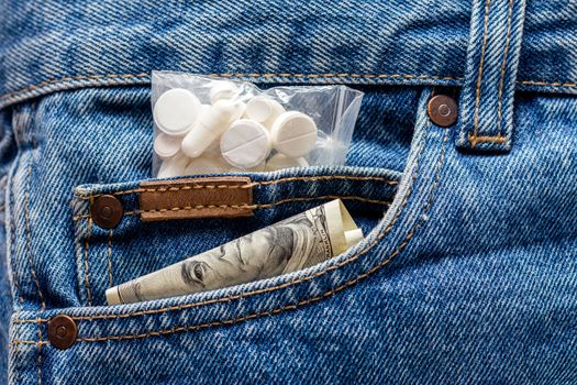 a hundred dollar banknote and pack of white pills sticking out from front pocket of jeans - close-up with selective focus