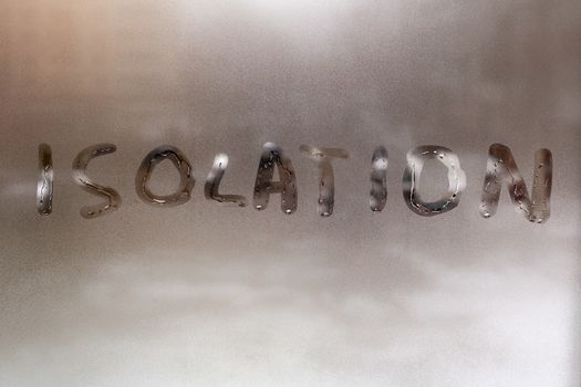 the word isolation handwritten on wet window glass at cloudy weather - close-up with selective focus and background blur.