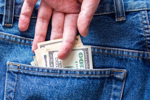 a hand taking hundred dollar banknote out from rear jeans pocket - close-up.