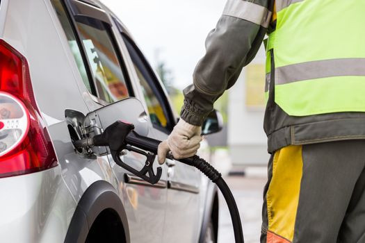 hand in white cotton fabric glove refueling gray metallic car on gas station - close-up with selective focus and blur