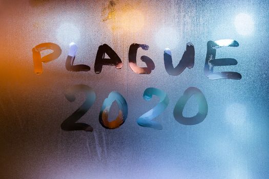 The words plague 2020 handwritten on sweat window glass surface at night. Pandemic concept.