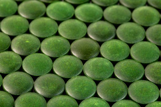 close-up background of many green organic spirulina tablets laid tight in one layer on flat surface.