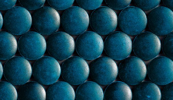 a seamless hexagonal pattern of many blue organic spirulina tablets laid tight in one layer on flat surface.