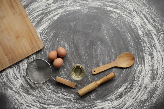 Chicken egg, flour, olive oil, kitchen tool on gray table background. Products for baking bakery products. Cutting board, rolling pin, flour sieve, wooden spoon. For bread or cake