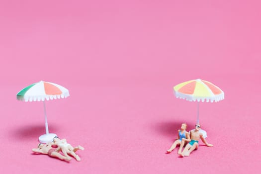 Miniature people wearing swimsuit relaxing on pink background , Valentine's day concept