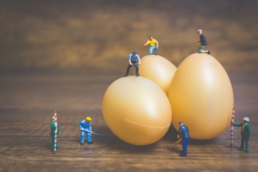 Miniature people work at Easter-eggs for Easter day on wooden background