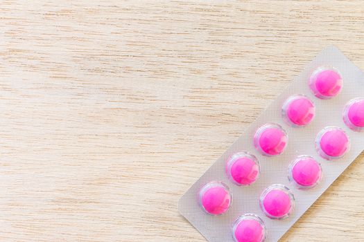 Pink pills in blister pack on wooden background