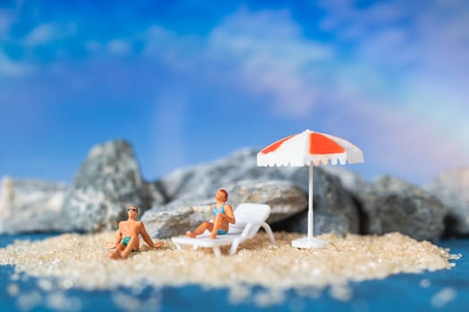 Miniature people wearing swimsuit relaxing on the beach with blue background , Summer time concept